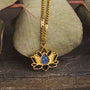 Collana "Balance" con un design di loto in oro con un centro lapis lazuli, impostato contro le foglie naturali.
