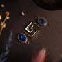 Orecchini a specchio con lapis lazuli e disegno in oro con uno stile geometrico su fondo scuro.