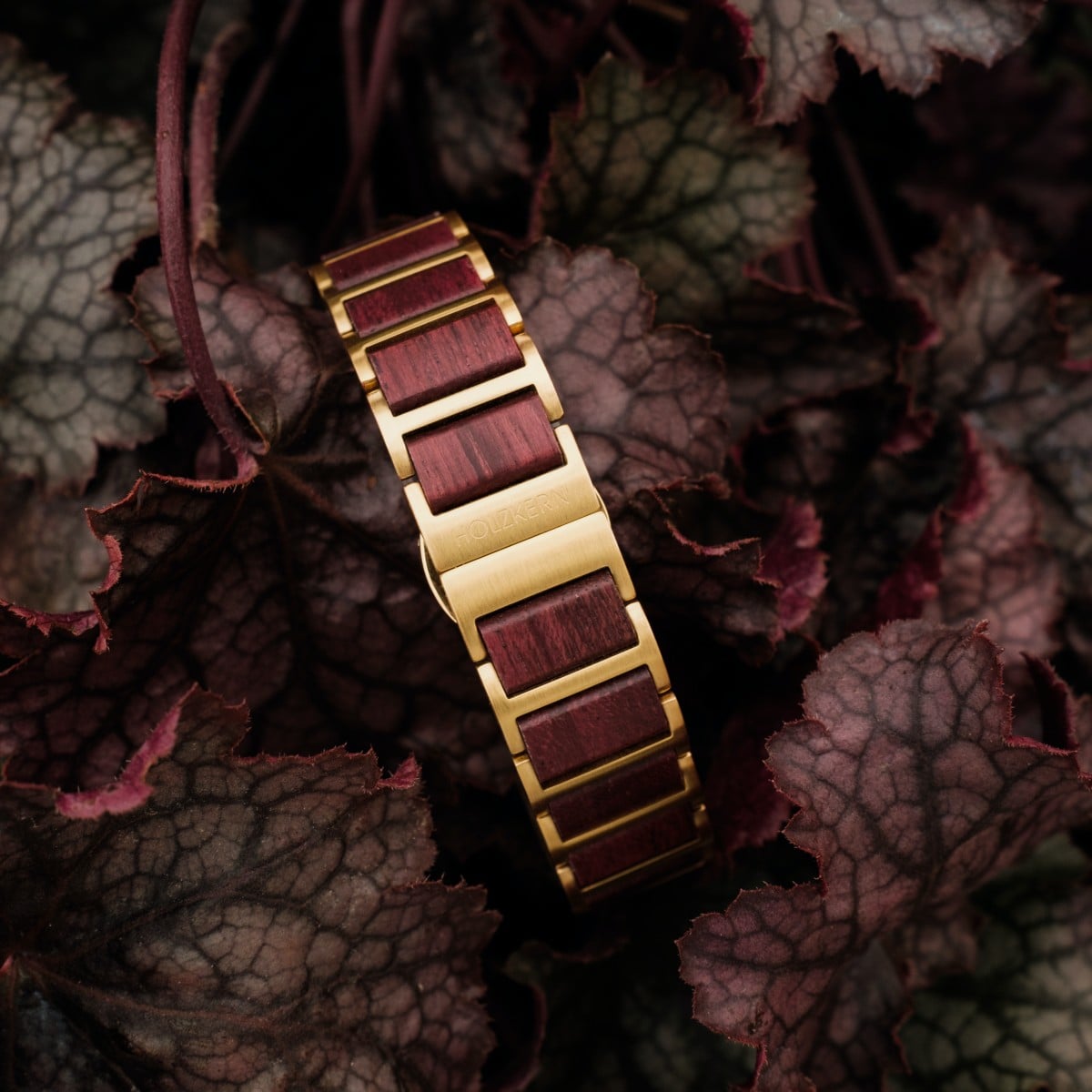 "Mauritius" watch bracelet with a luxurious amaranth and nacre design, set against rich foliage.