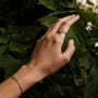 Anello "Visual Ring", con anelli di colore grigio e argento, indossato su fondo verde lussureggiante per un look elegante.