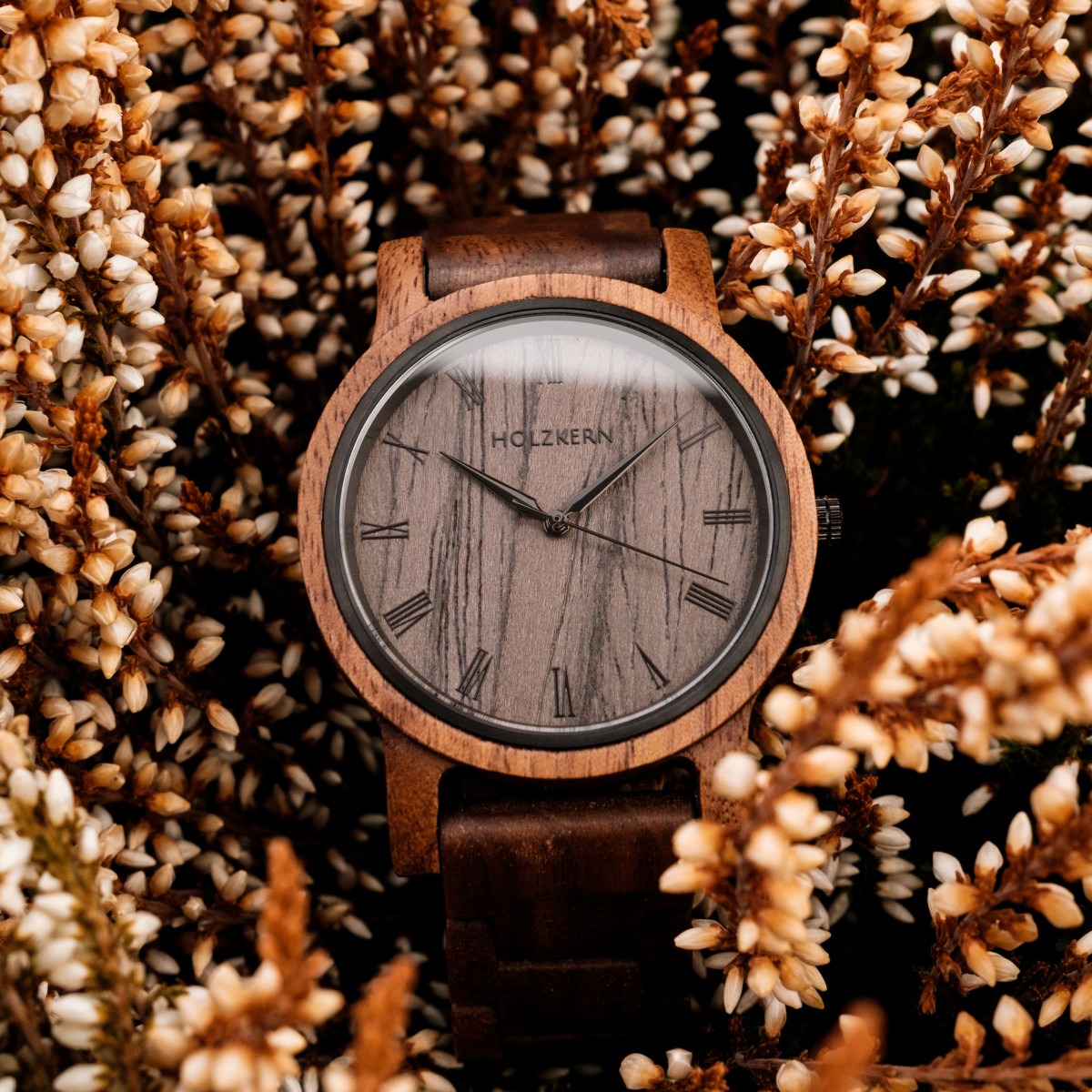 "Spring Evening", un elegante orologio in legno, presenta un design in noce naturale e legno di piombo, ambientato su uno sfondo di fogliame rustico.