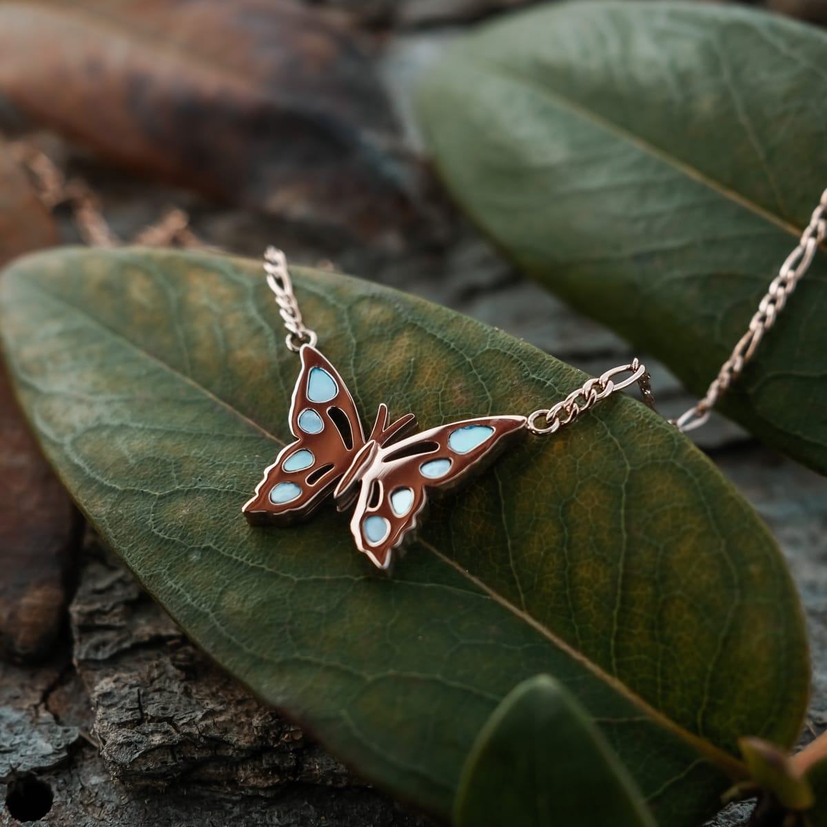 "Fritillary Necklace", a delicate butterfly necklace in nacre and rose gold, elegantly styled on a leaf background.