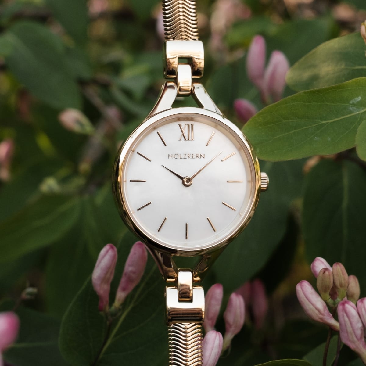Elegante orologio "Kaliya" con un viso nacre e accenti d'oro, in stile con uno sfondo floreale.