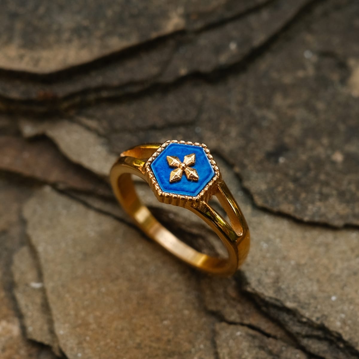 "Spectral Ring": un anello in oro con un centrotavola blu con un design intricato, impostato su uno sfondo in pietra naturale.