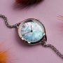 Orologio "Brighter" con un viso nacre e accenti d'argento su uno sfondo viola vibrante.
