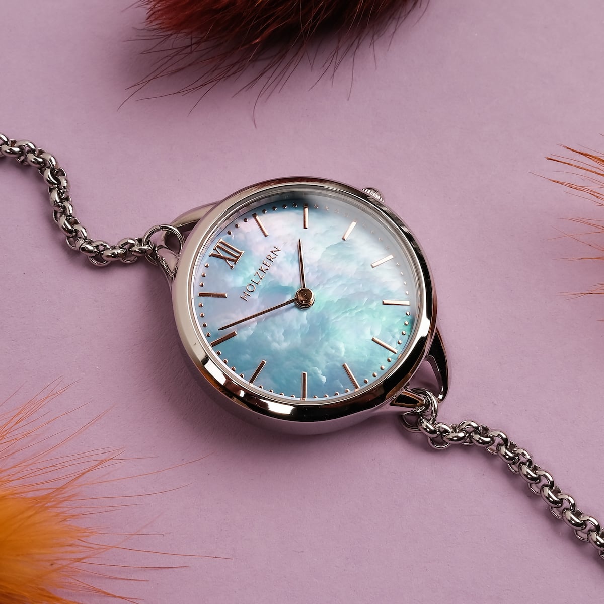 Orologio "Brighter" con un viso nacre e accenti d'argento su uno sfondo viola vibrante.