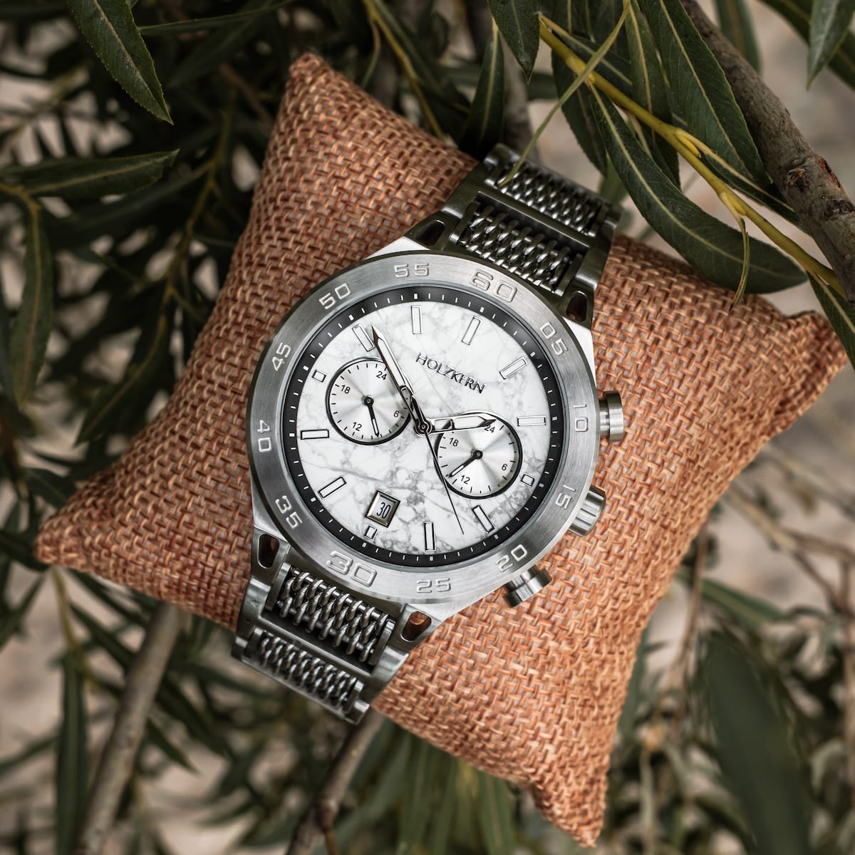 "Elqui" watch featuring a marble-style face and silver accents on a natural woven cushion.