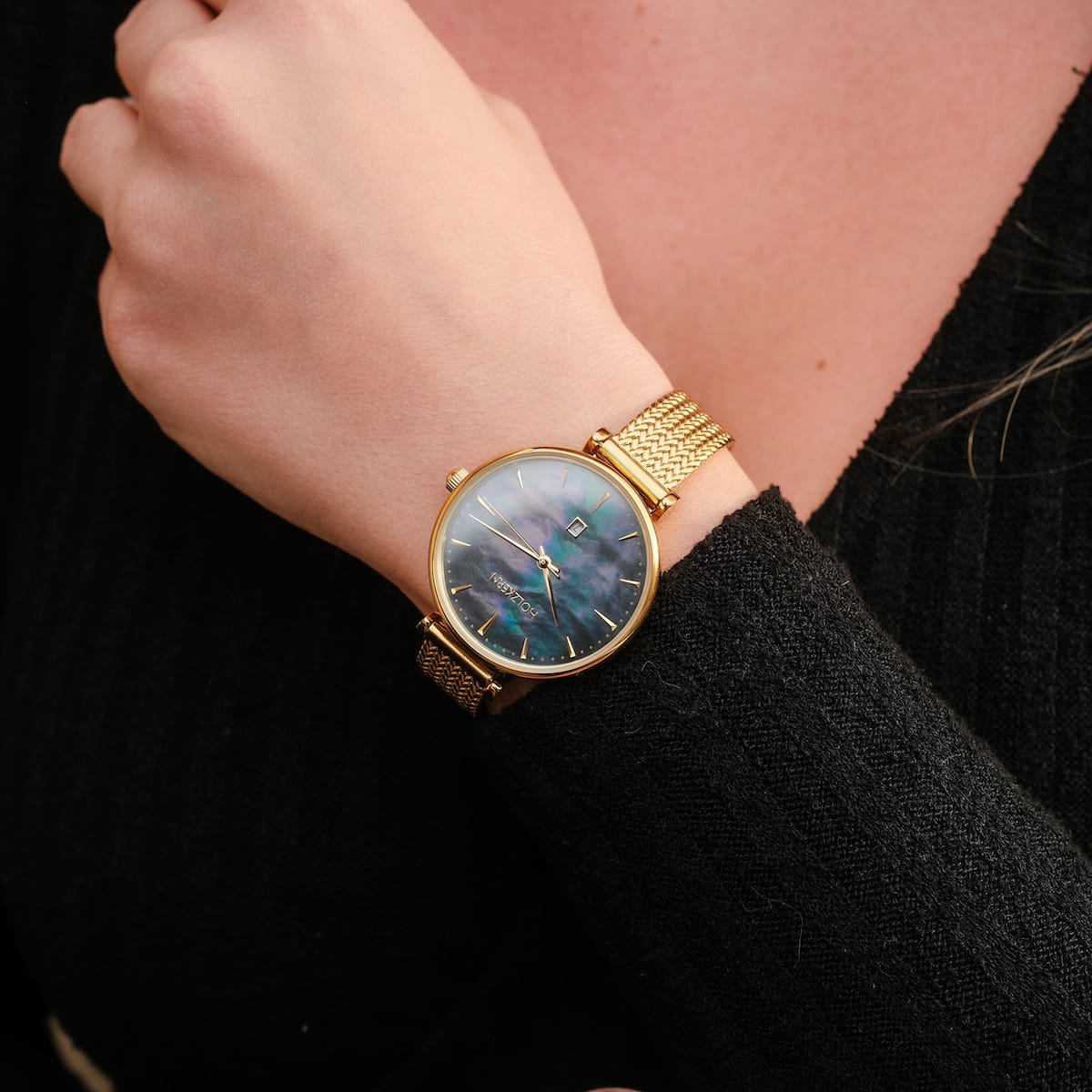 "Giggles", un orologio elegante con un quadrante nacre e bracciale in mesh oro-tono, indossato su un polso.
