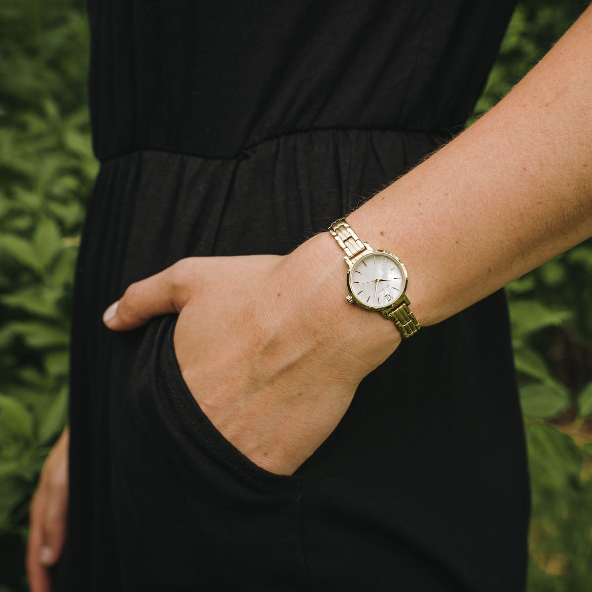 "Hanwi" watch featuring a nacre dial and gold band on a wrist, showcasing elegant style against a natural backdrop.