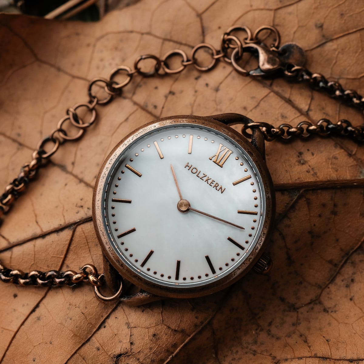 "Touching" watch with nacre dial and antique copper finish on a leaf background.