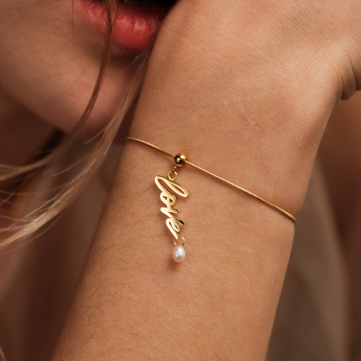 Bracciale "Love-Charm" con un elegante fascino in oro con un accento di perla, indossato con grazia al polso.