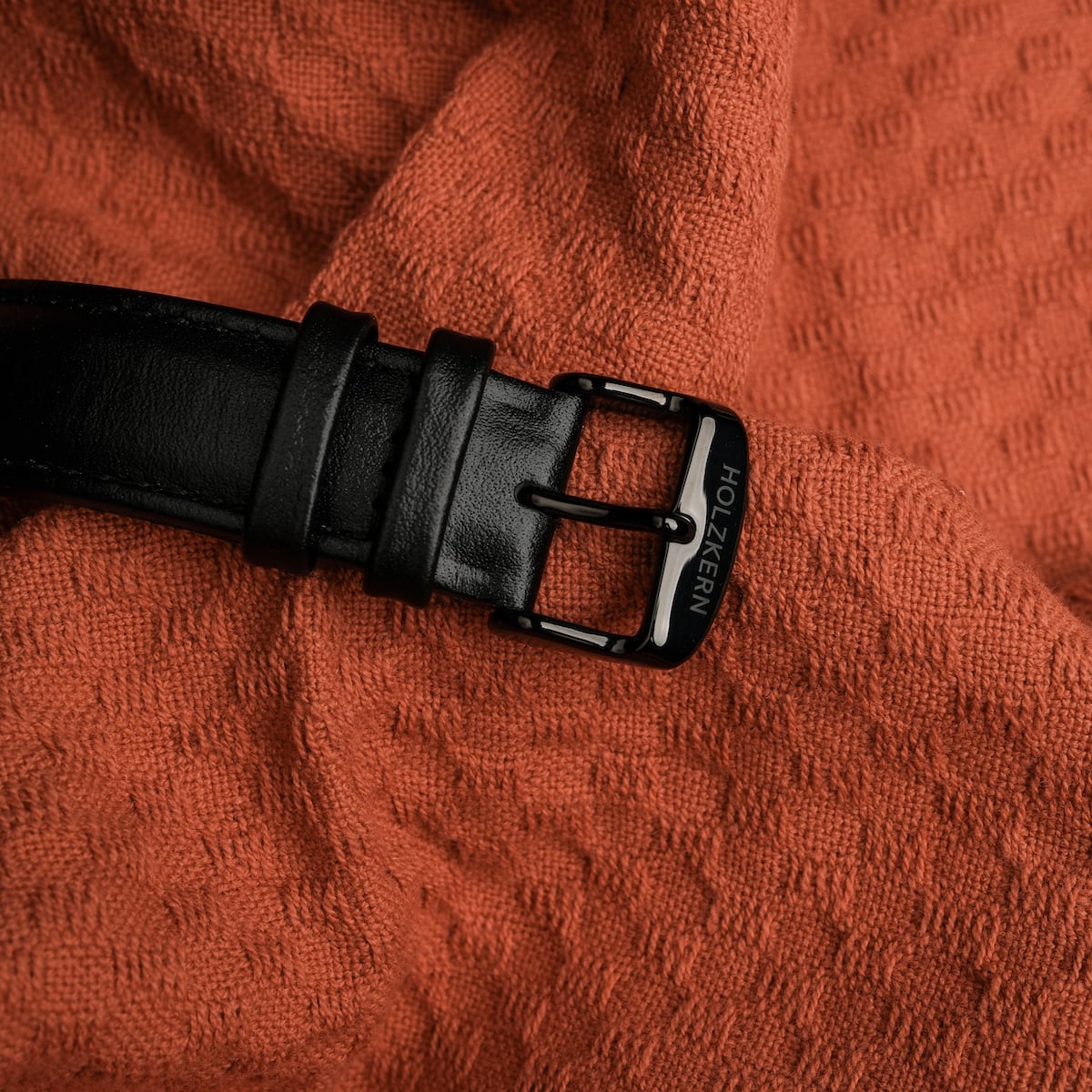 "Rackets belt featuring a sleek black buckle, styled on textured orange fabric."