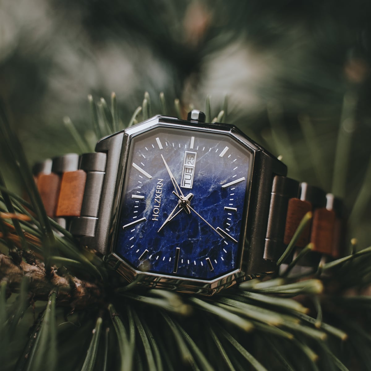 Orologio "Moneo" con design in koa e marmo con accenti in argento su uno sfondo naturale.