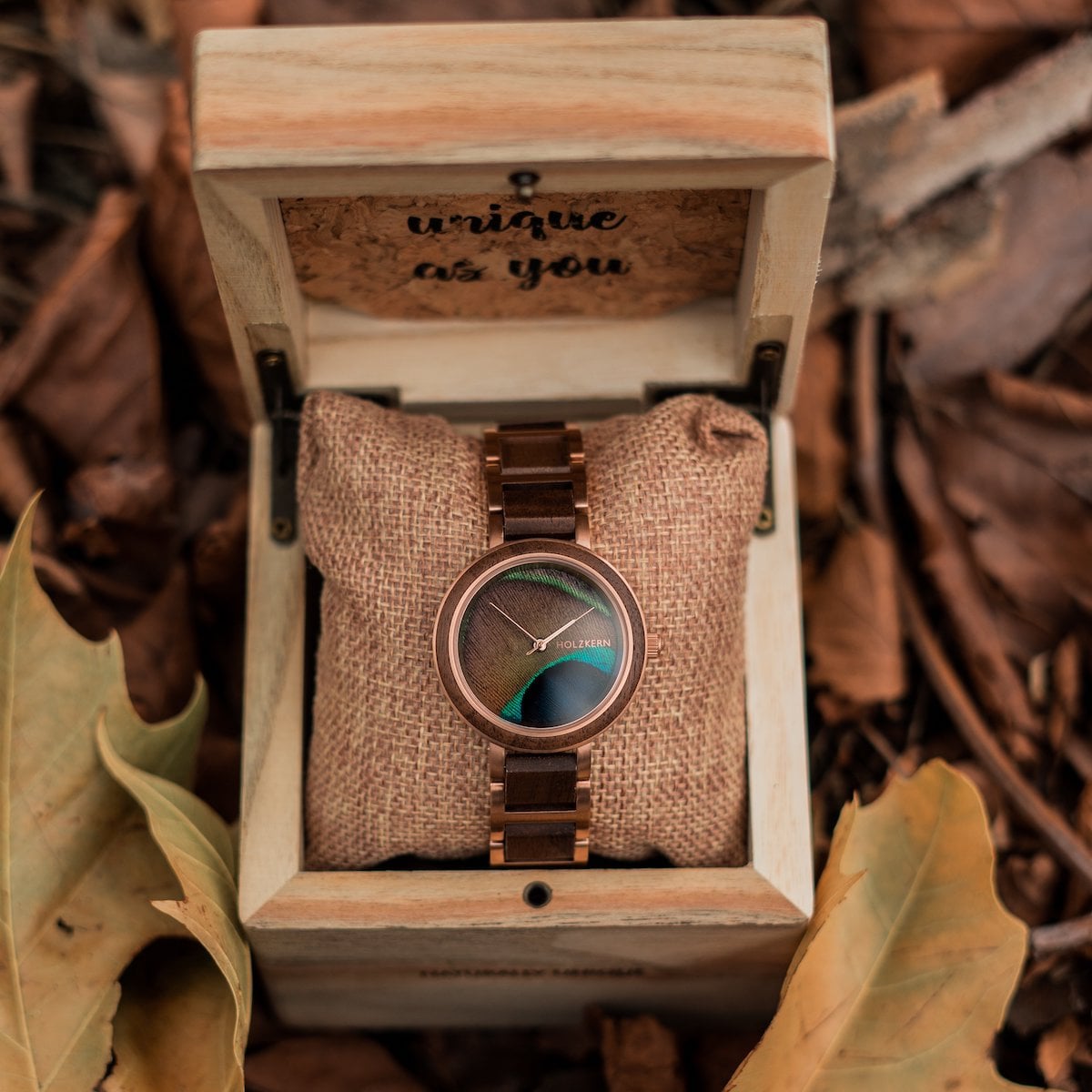 "The Optimist" watch featuring walnut wood and a peacock feather dial, displayed elegantly in a rustic wooden box.