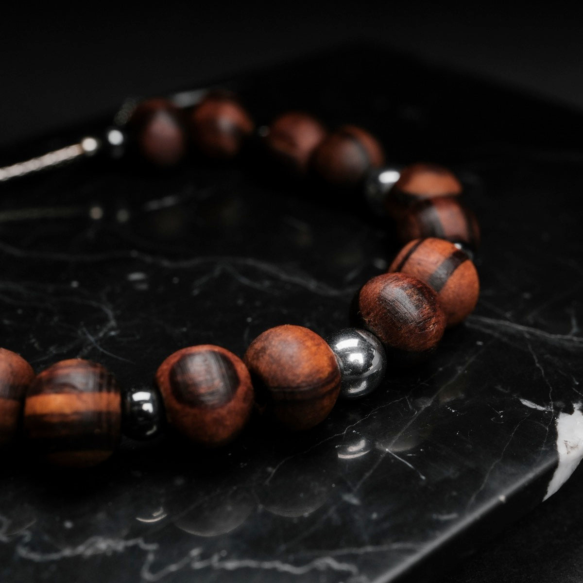"Superset", un braccialetto elegante, presenta perline di noce e ematite su uno sfondo di marmo scuro.