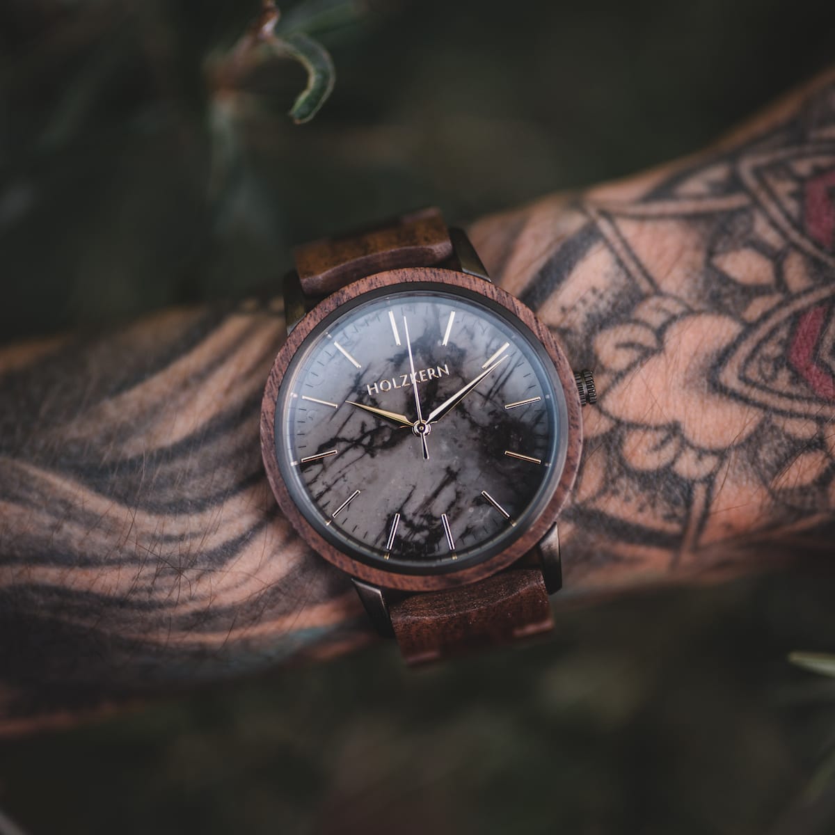 Orologio "Leonardo" con un design in noce e marmo su un polso tatuato, che evidenzia la sua eleganza rustica.