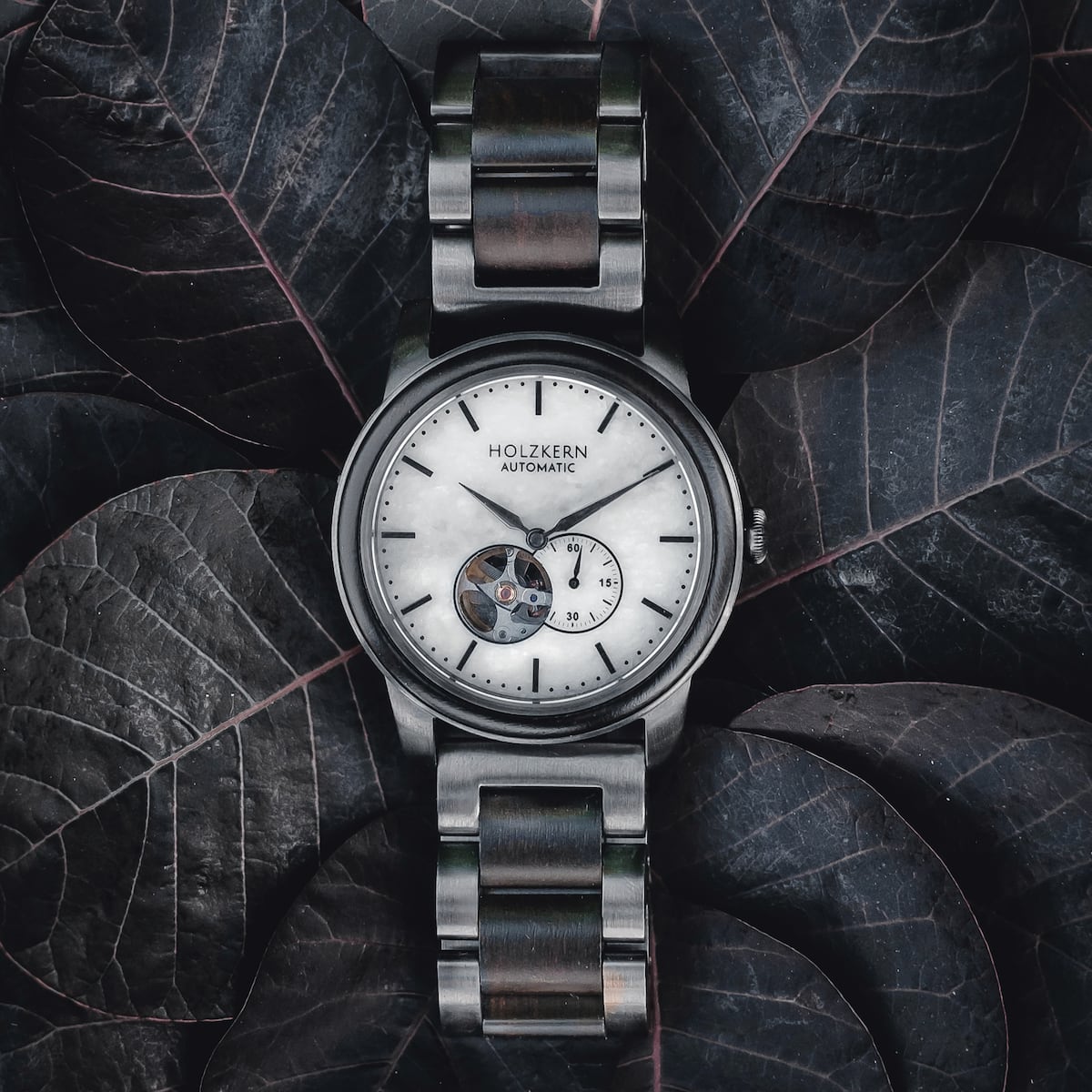 Orologio "Manhattan" con disegno acero e marmo, caratterizzato da un'estetica elegante e moderna su uno sfondo foglia scuro.