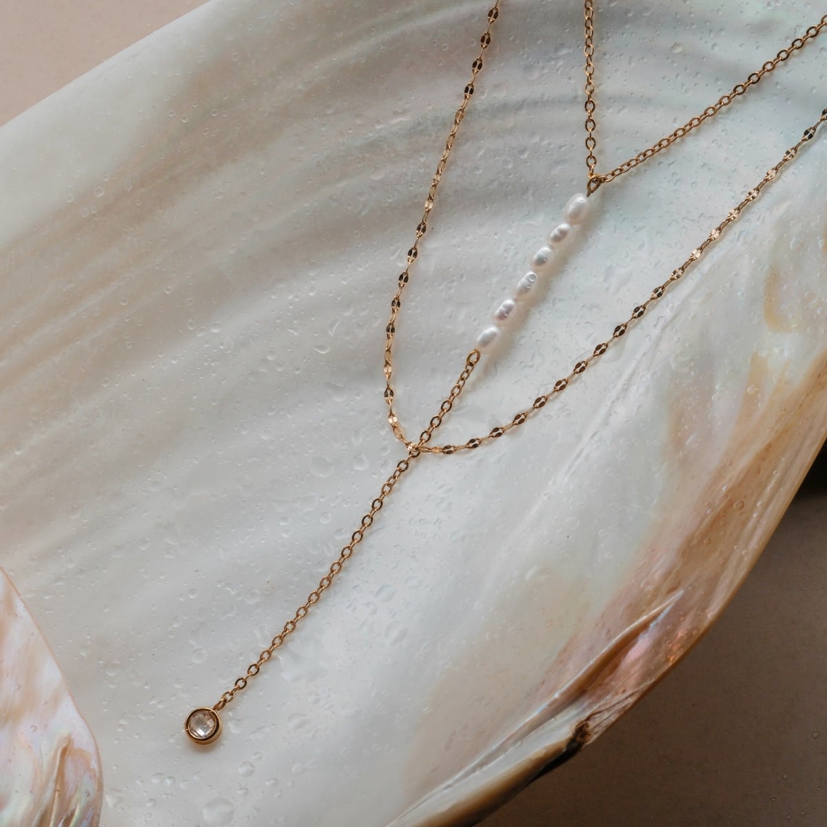 "Collana di estate", una collana delicata con perle e zirconi su una catena d'oro, esposta su un'elegante superficie di conchiglia.