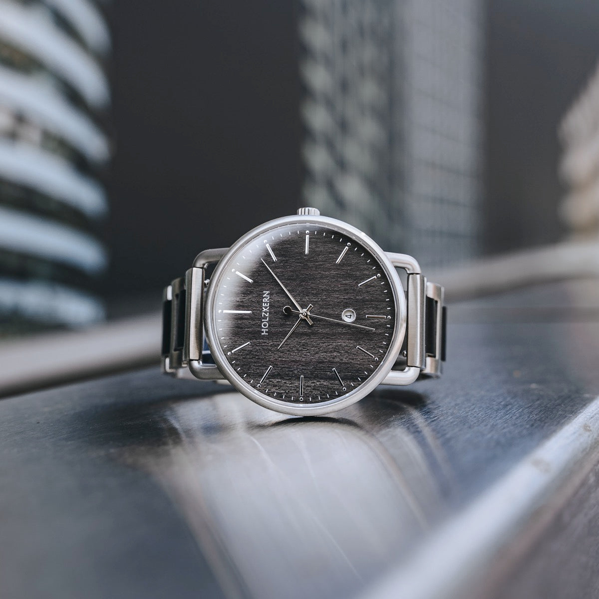 Orologio da polso "Odaiba" elegantemente caratterizzato da un quadrante acero e design elegante, ambientato su uno sfondo urbano.