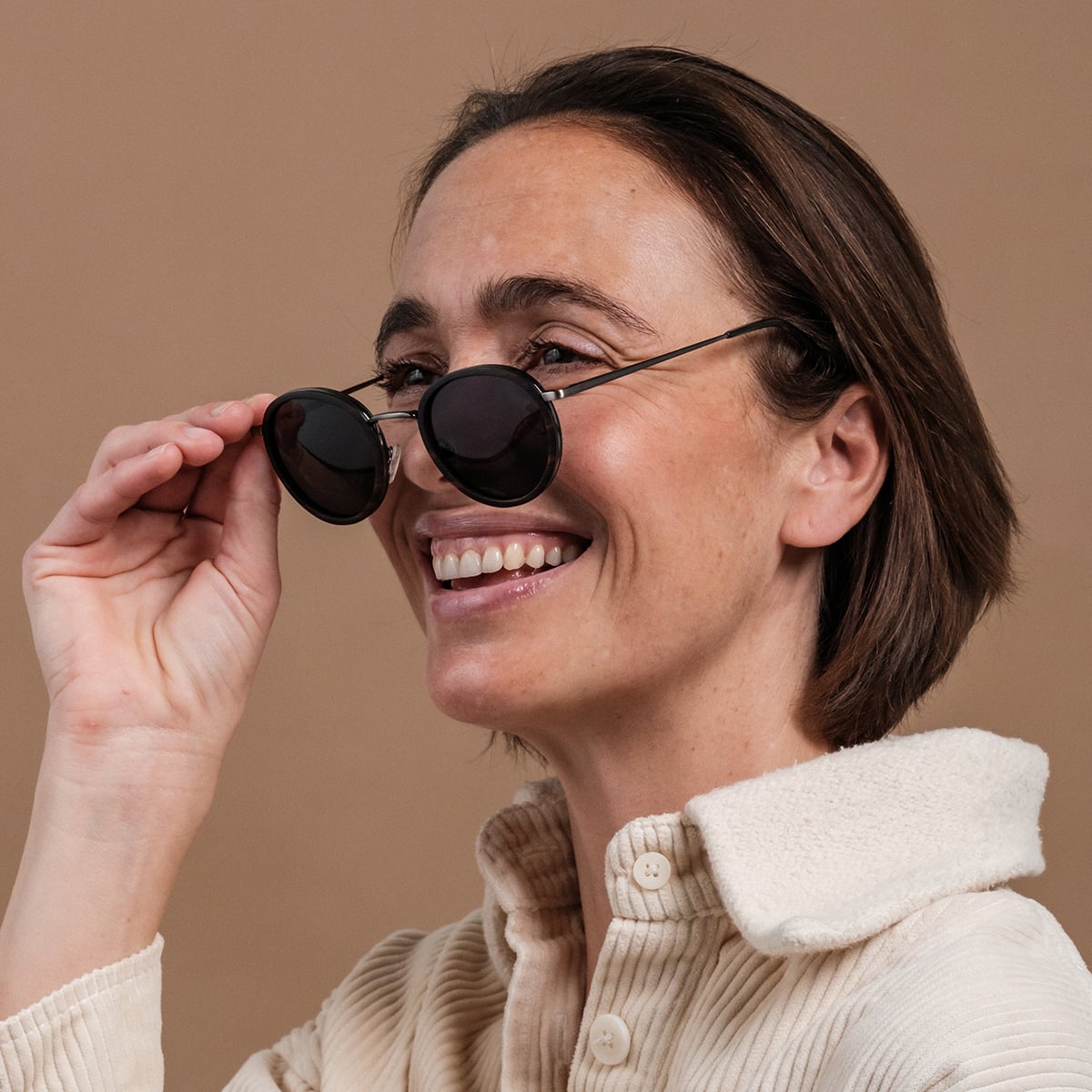Gli occhiali da sole "The Radiant M" caratterizzati da un design elegante in legno di piombo e argento antico, indossati da una donna sorridente.