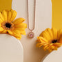 Collana "Suncatcher", con ametista e oro rosa, elegantemente modellata su un fondo floreale luminoso.