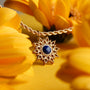 "Collana Suncatcher": Elegante collana in oro con un design sunburst con centro lapis lazuli, circondato da fiori gialli vibranti.