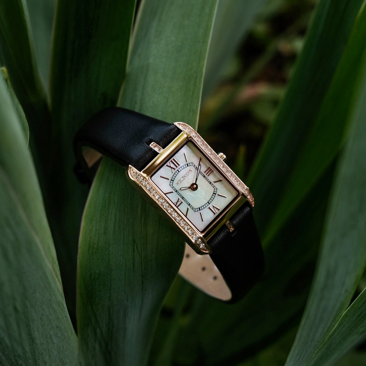 Orologio "Memoire" con un viso e cinturino nero intarsiati, elegantemente progettato con un quadrante rettangolare e accenti in oro.
