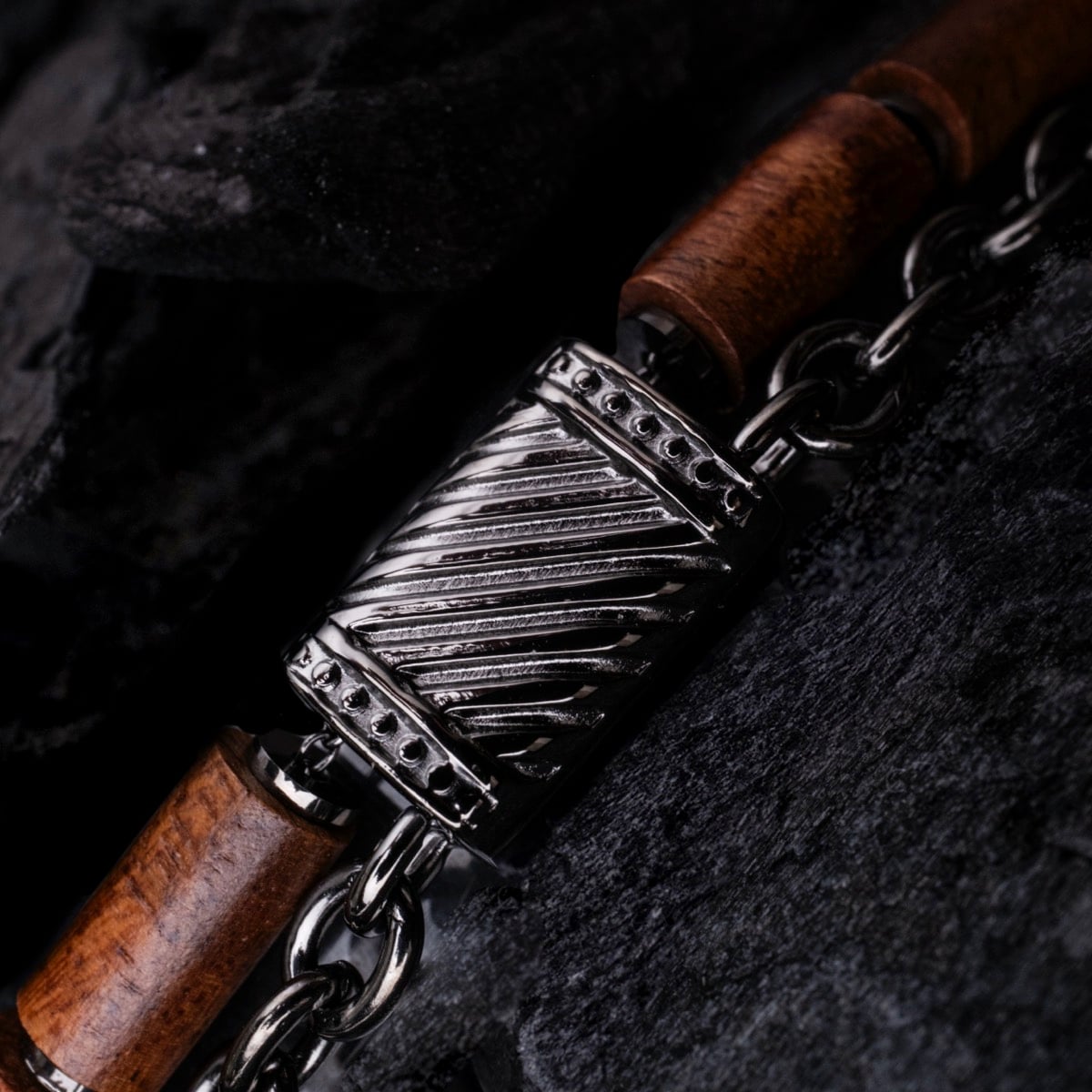 Bracciale "Supersonic" con un design in legno di koa e metallo grigio contro rocce nere strutturate.