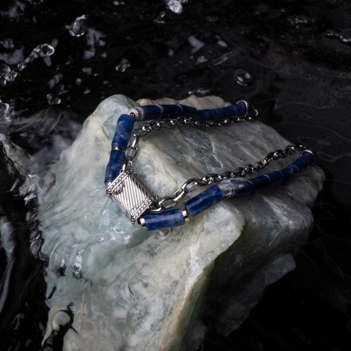 "Supersonic" necklace, crafted with a sleek marble and silver design, elegantly displayed on a textured stone surface.