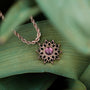 "Collana di Suncatcher", una collana di abbronzatura in oro rosa con un centrotavola ametista, esposta contro il fogliame verde.