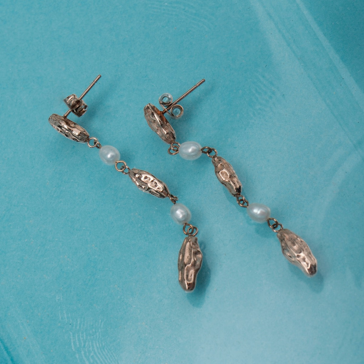 "Summersweet Earrings I: Elegantly styled pearl and rose gold earrings on a blue background."