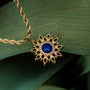 "Collana di Suncatcher", una collana d'oro con un ciondolo lapis lazuli, incastonato contro foglie verdant per un contrasto elegante.
