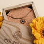 "Collana di Suncatcher", una collana d'oro con lapis lazuli, visualizzata con eleganza con fiori e una scatola di legno.