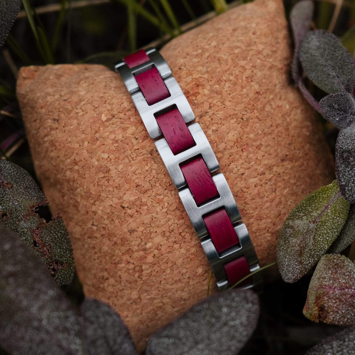 "Acoustic" bracelet showcasing an amaranth and silver design on a textured cushion surrounded by foliage.