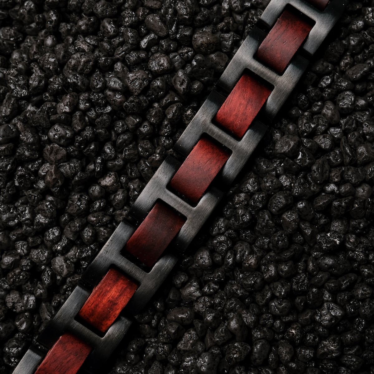"Acoustic" bracelet featuring a Padauk wood and black metal link design on textured black gravel.