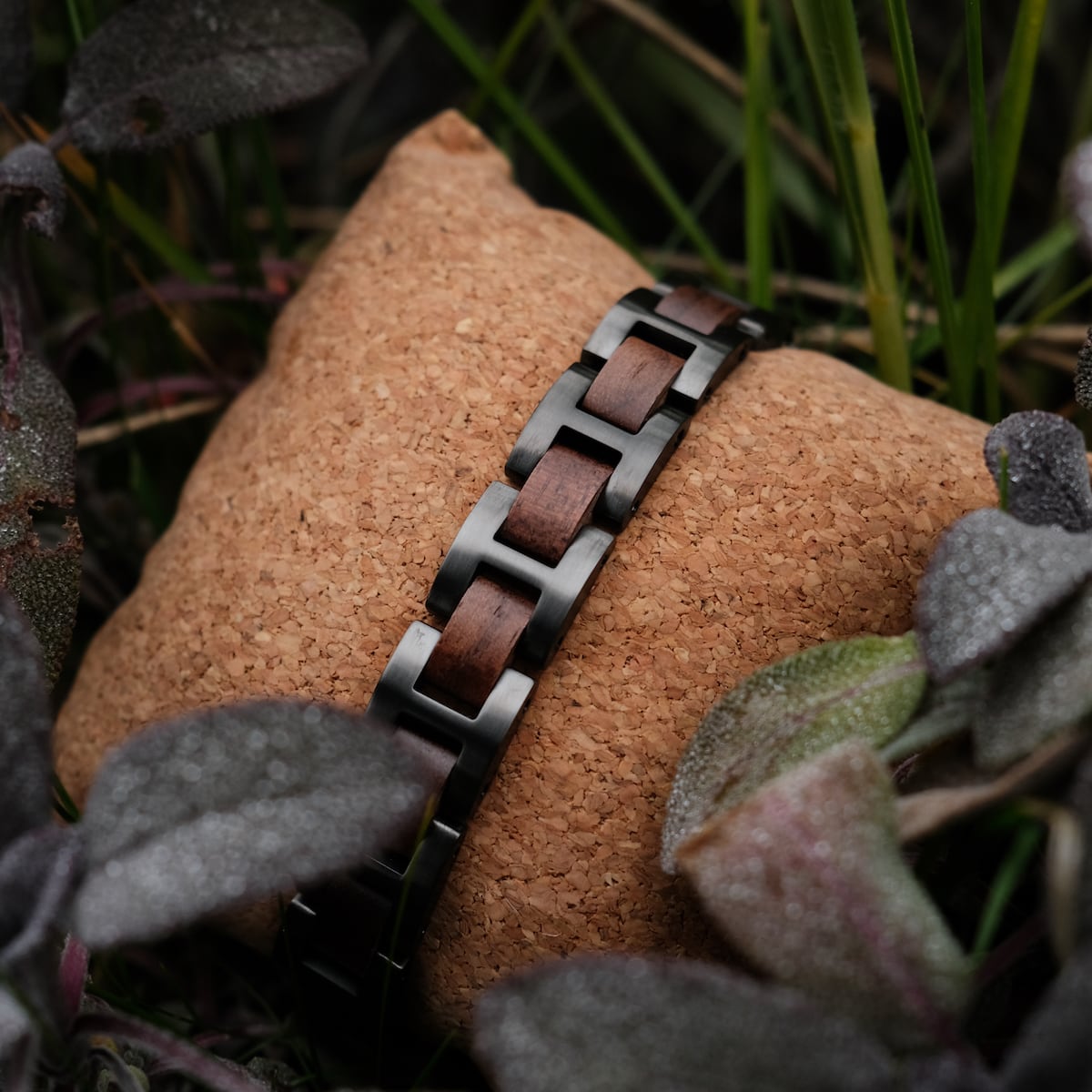 "Acoustic" bracelet, featuring a walnut and grey design, displayed on a textured cushion among foliage.