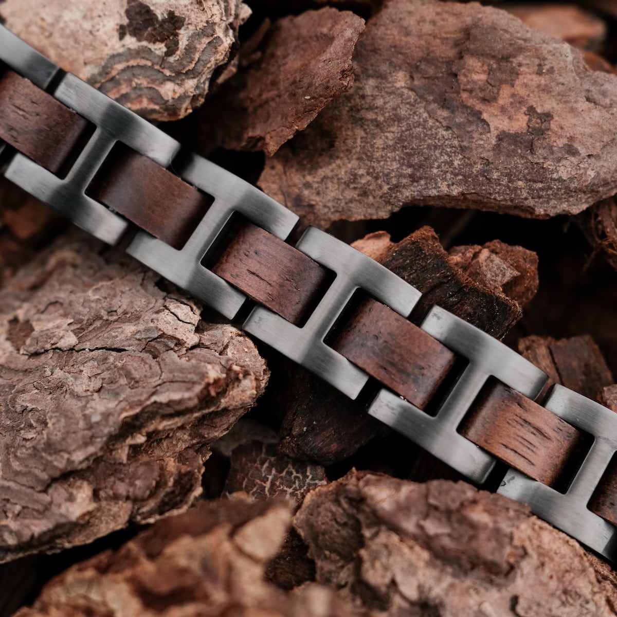 "Acoustic", a stylish bracelet with a walnut and grey metal design, resting on earthy bark.