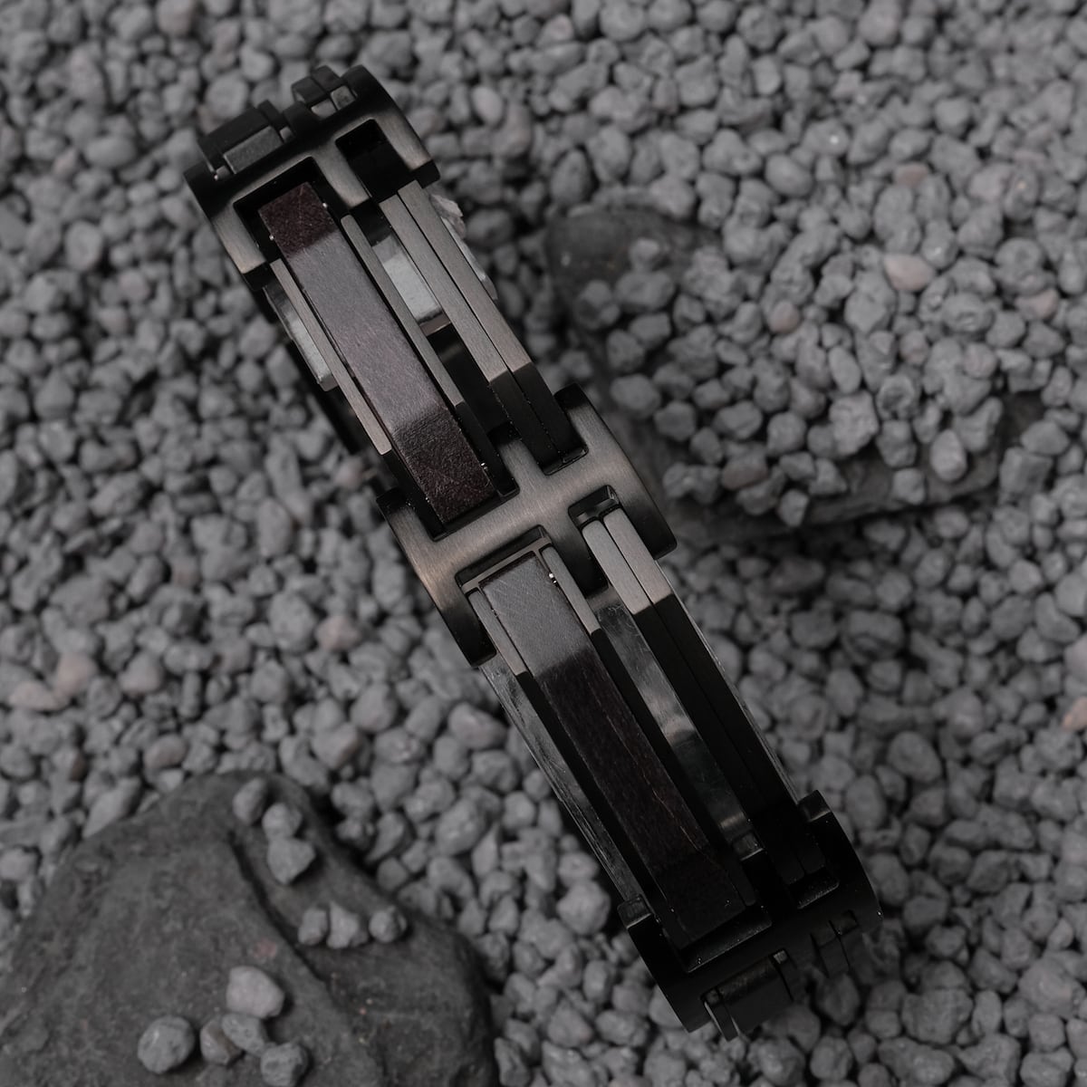 "Staccato", un bracciale in acero e nero, presenta un design elegante e moderno su uno sfondo roccioso.