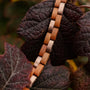 "Rondo" bracelet in cherry and rose gold hues with a natural, elegant design intertwined with dark leaves.