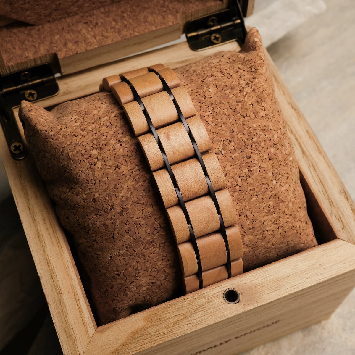 Orologio "Grandezza" con acero e viola scuro, elegantemente esposto su un cuscino di sughero all'interno di una scatola di legno.