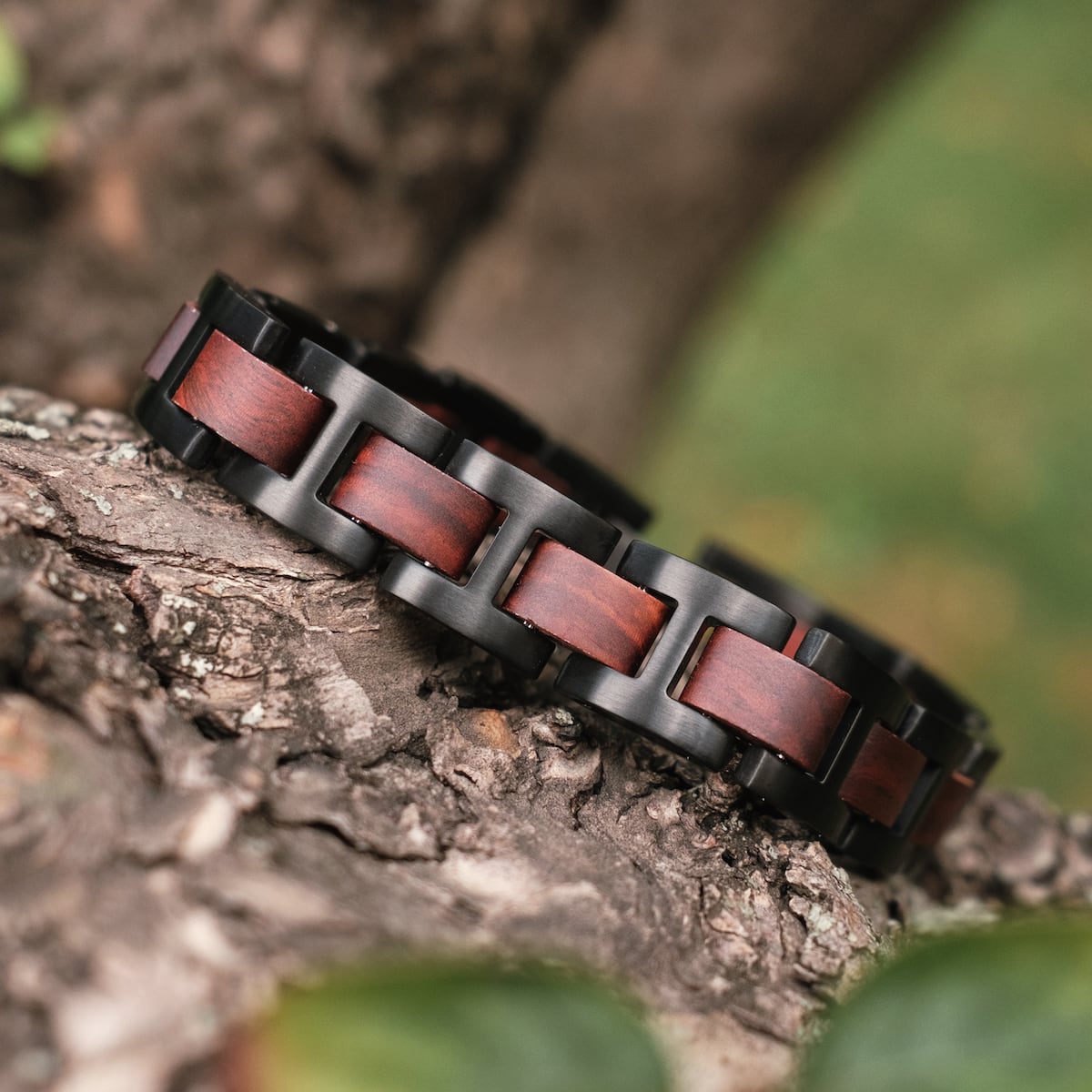 "Acoustic", a stylish bracelet with padauk wood and black metal links, displayed outdoors on a tree branch.