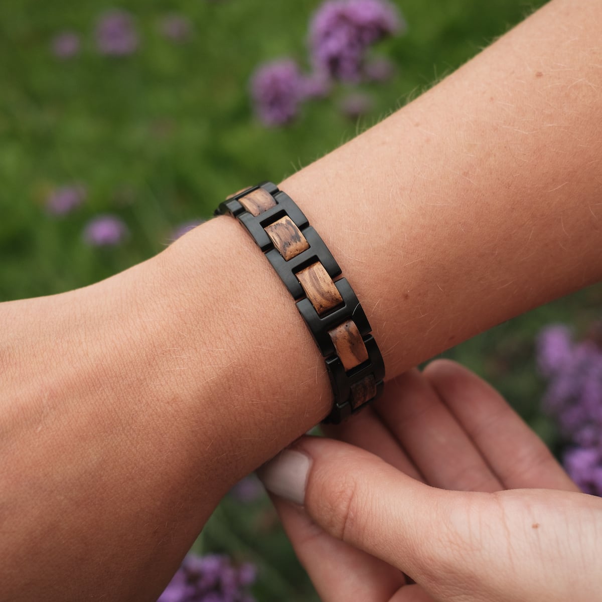 Bracciale "acoustico", con zebrawood e design nero, indossato al polso tra fiori viola.