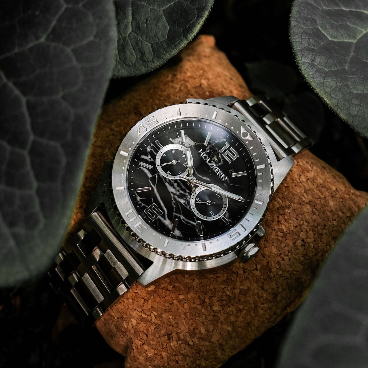 "Norium watch featuring a marble dial and silver accents nestled among textured leaves."