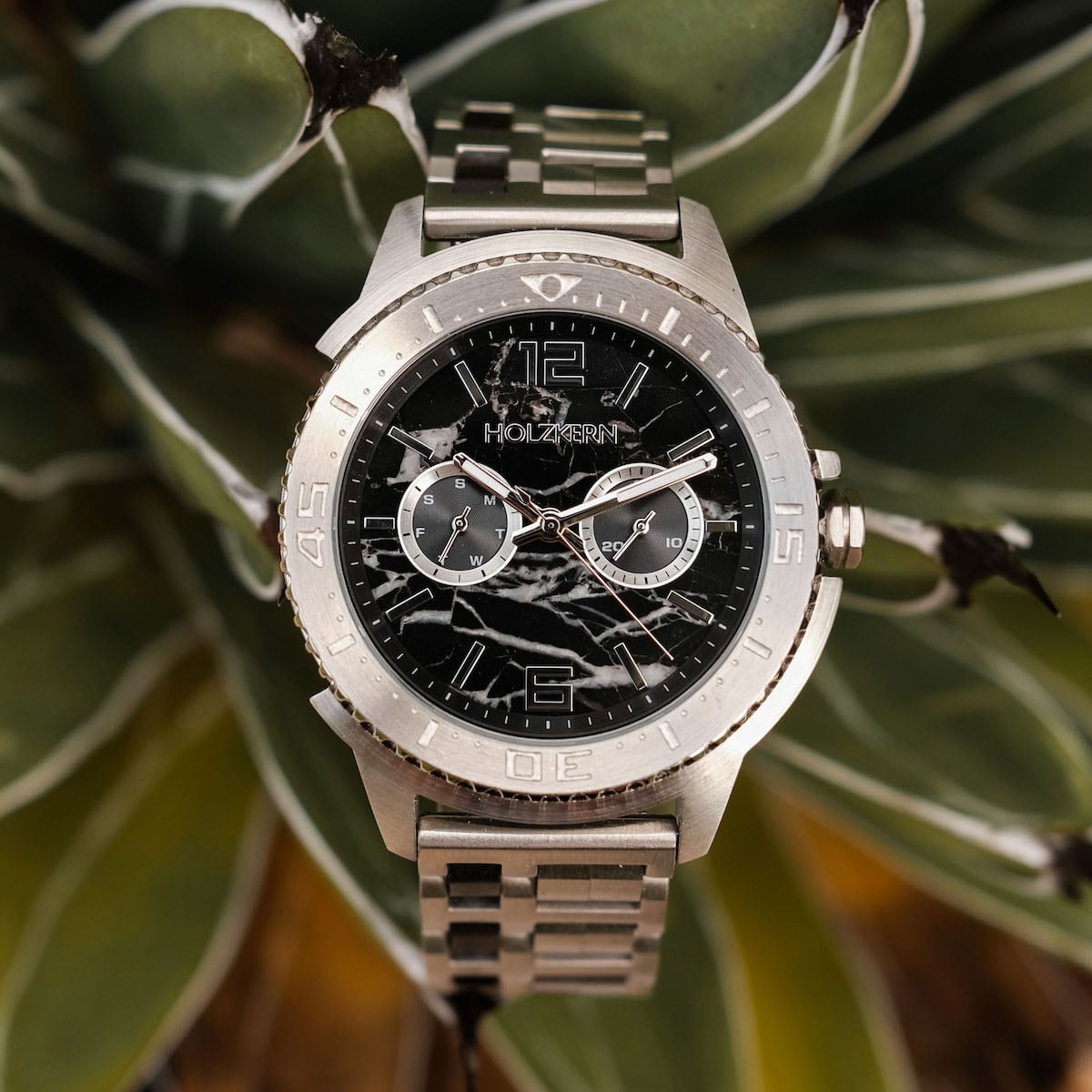 "Norium watch featuring a marble dial and silver bracelet, set against a blurred natural background."