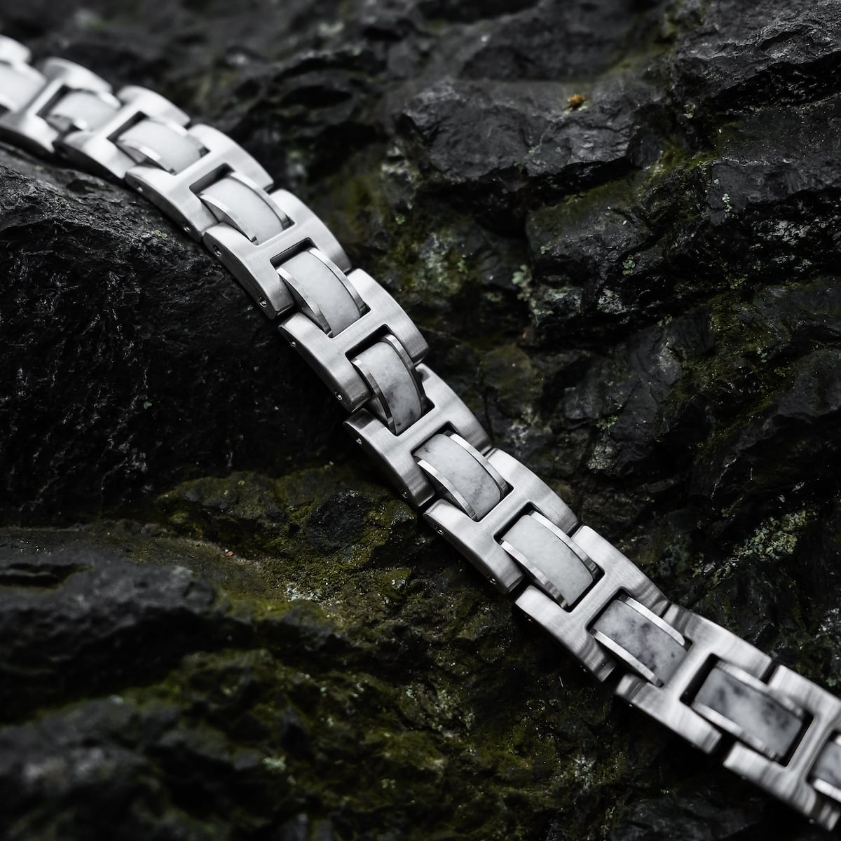 "Forte" bracelet in marble and silver with a sleek, modern design displayed on a rock surface.