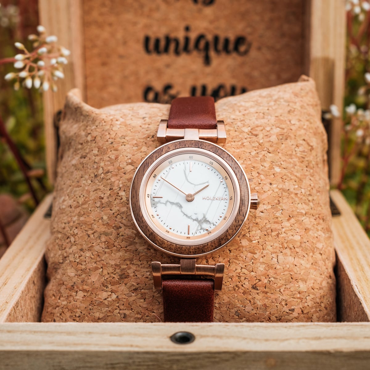 "Ida" watch with a walnut and marble design, featuring a brown leather strap in a rustic wooden setting.