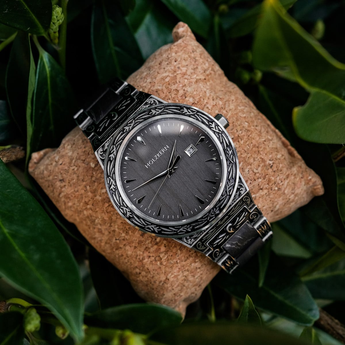 Orologio "Misir" con dettagli intricati e uno stile acero sofisticato su un cuscino immerso nel verde.