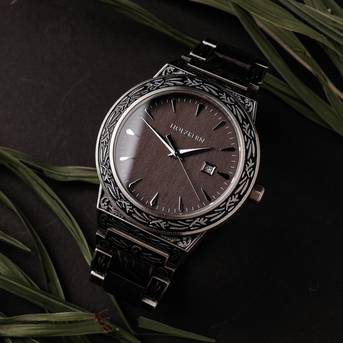 Orologio "Misir" con incisioni intricate e finitura acero, caratterizzato da un quadrante scuro elegante.